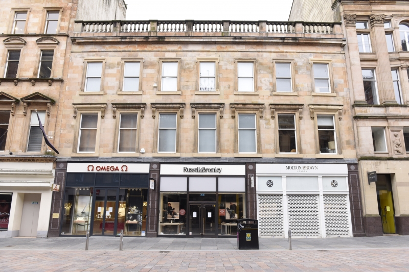 Three storey blond sandstone building with ballustrade, three shops at ground floor level