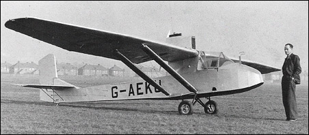 Two seater glider on the ground, with high wing, and an engine mounted above the wing.