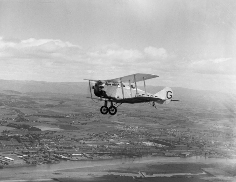 Bristol biplane trainer in flight over Renfrew. Beardmore's shipyard visible behind, with Singer's factory to the right.