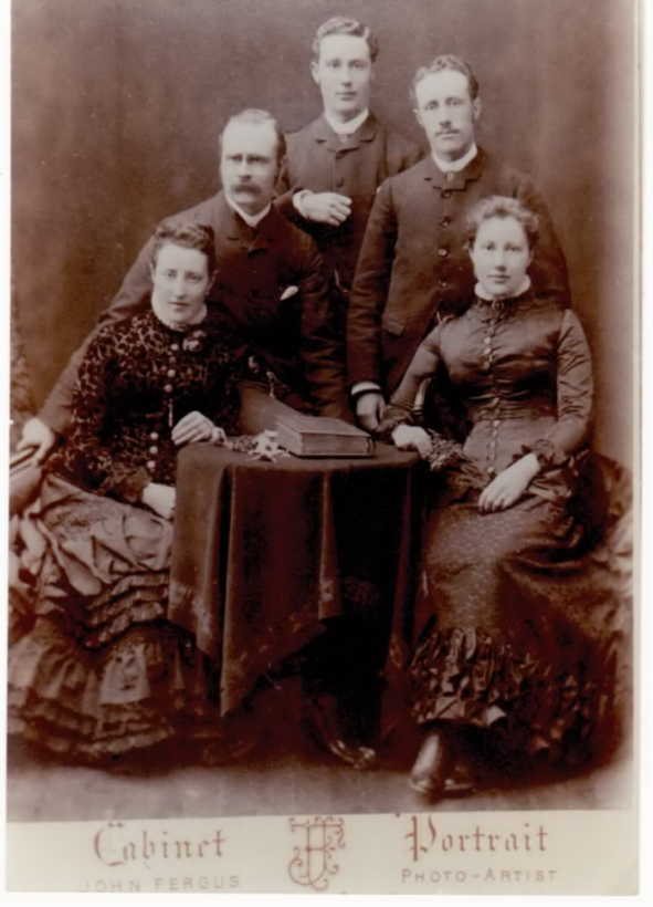 Two young women seated, their three brothers standing behind