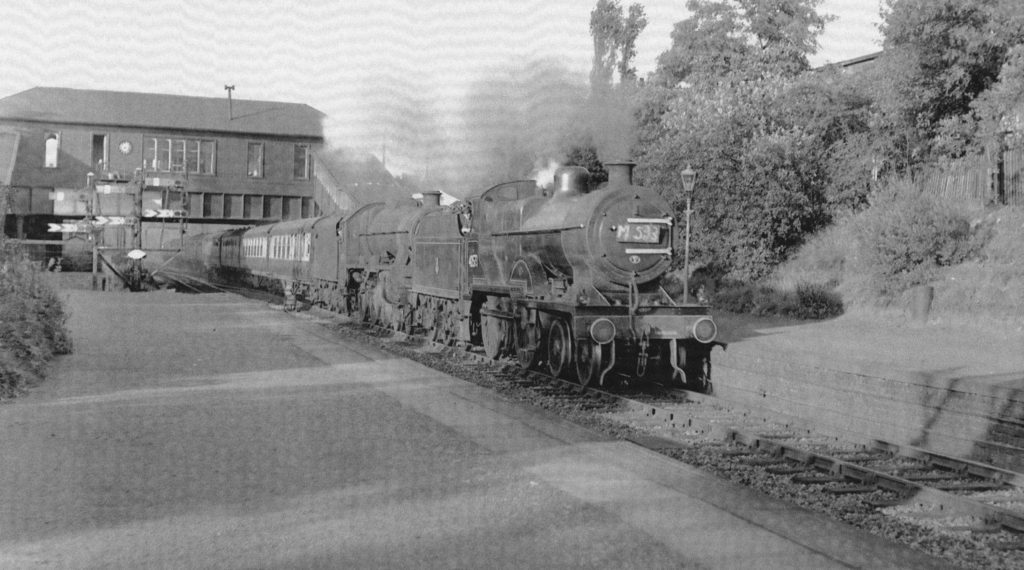 Two steam engines pulling a train southbound through the station
