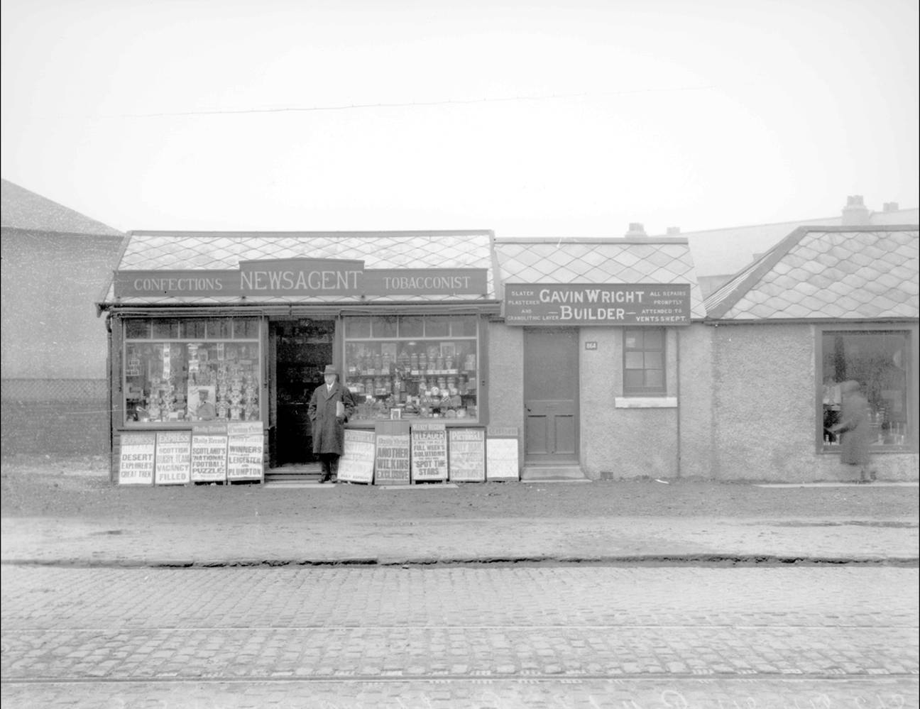 Man stands outside single storey newsagent building. Gavin Wright's builder's office next door