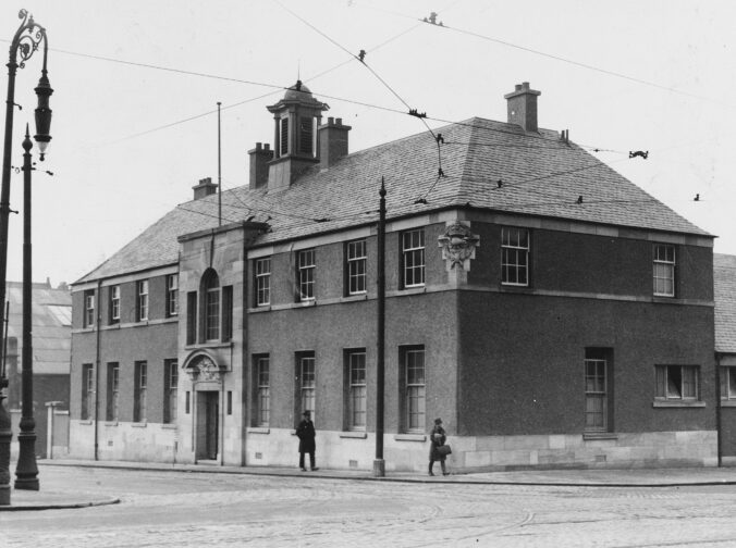 Two storey rendered building with a stone facade over the entrance, featuring the RAF badge. A further badge wraps round the corner under the eaves