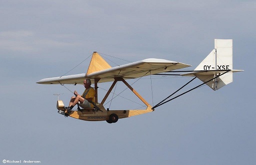 Small glider in flight. Pilot sits very exposed at the front, no canopy, just a seat and a wooden skid underneath. Rather him than me.