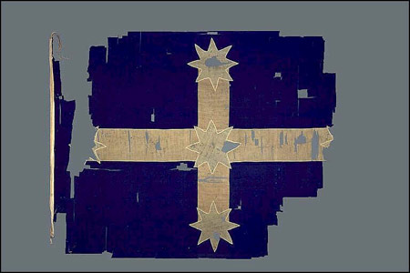 Tattered flag with missing sections, white cross on blue, with white star at the points of the cross