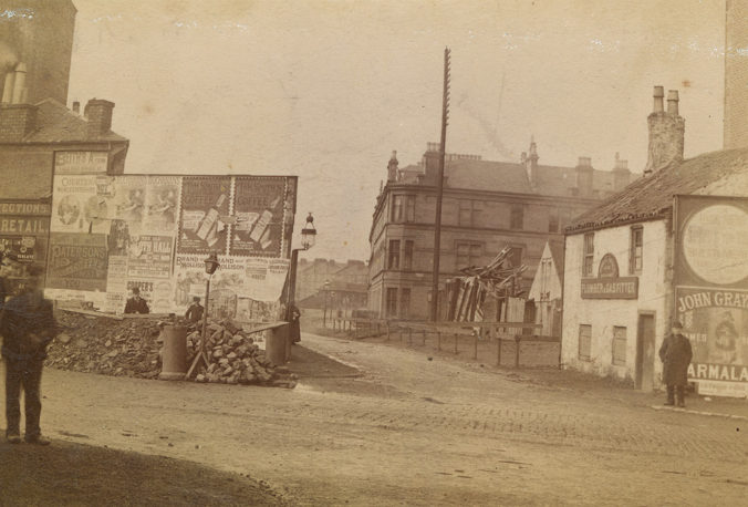 Sepia photo of advertising hoardings and buildings at mouth of Nithsdale Street